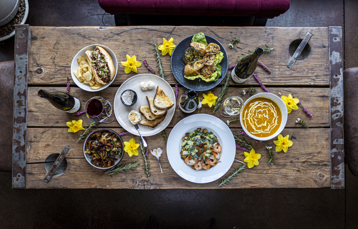 A rustic wooden table filled with various dishes and seasonal flowers. 