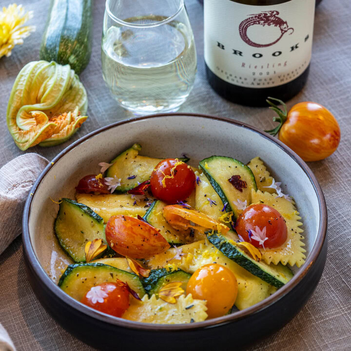 An end of summer bounty! A bowl of pasta with sauteed zucchini and tomatoes paired with a glass of chilled white wine from Brooks Wines.