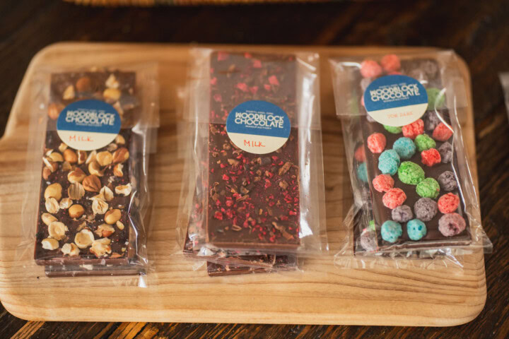 A wooden board serves up a selection of adult Halloween chocolate bars each decorated with either crushed hazelnuts, dried rose petals, or colorful, fruity cereal puffs.