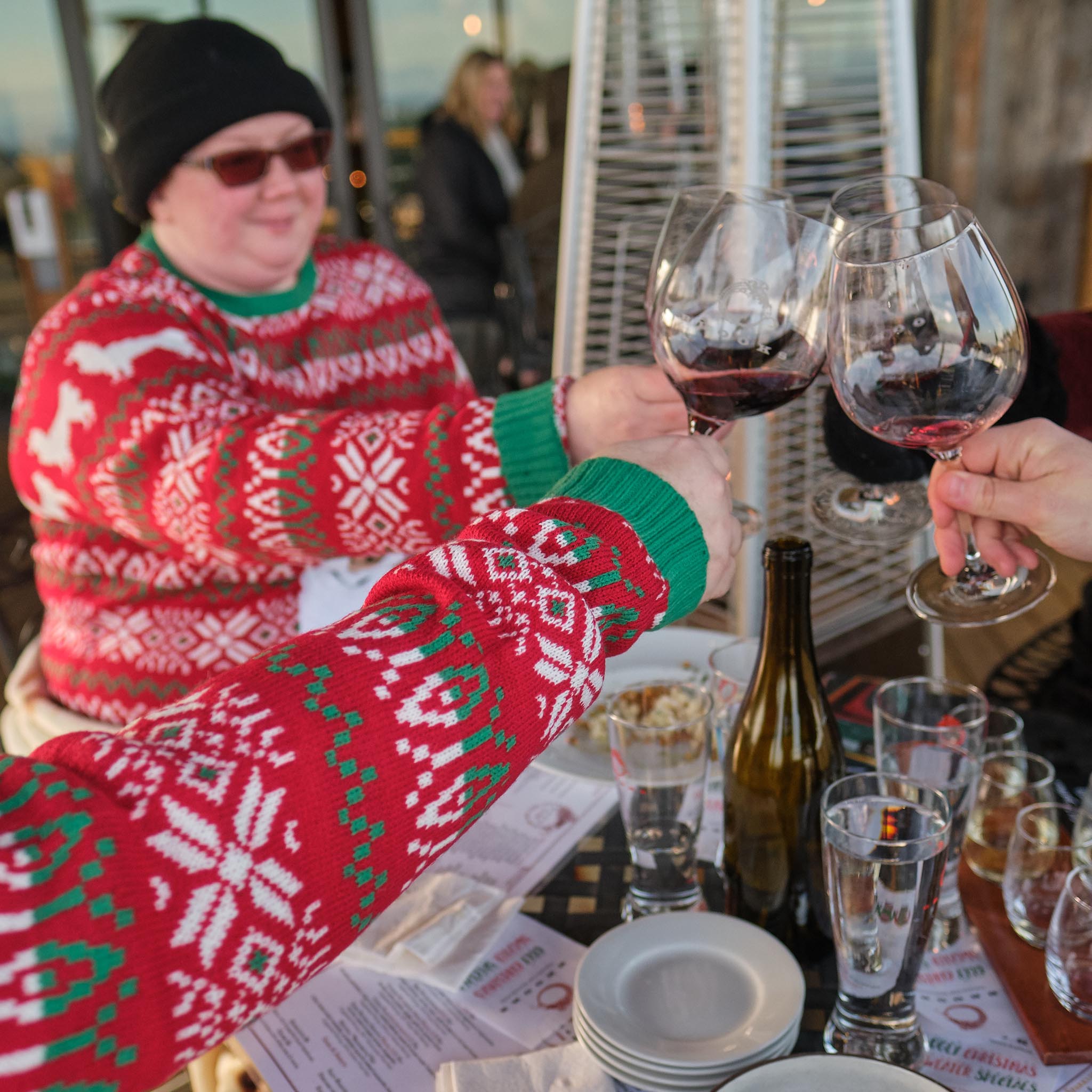 A woman dressed in a bright red Christmas sweater, clinking glasses with similarly dressed friends.