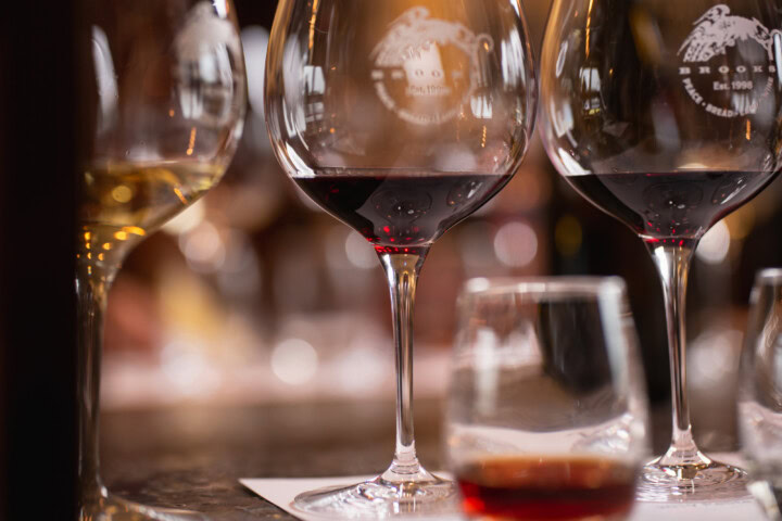 A flight of wine in stemmed glasses includes a glass of white wine, two glasses of red wine, and a small stemless glass of an aged red wine. 