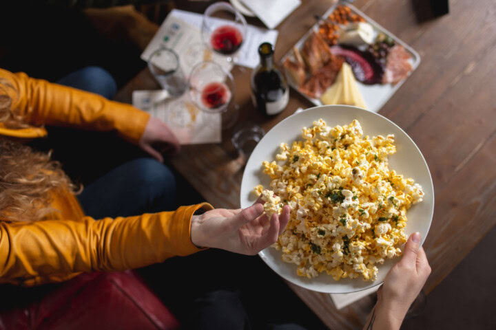 Friends dressed in Halloween orange long sleeve shirts grab handfuls of savory popcorn with herb oil along side glasses of Pinot Noir from Oregon's Willamette Valley. 