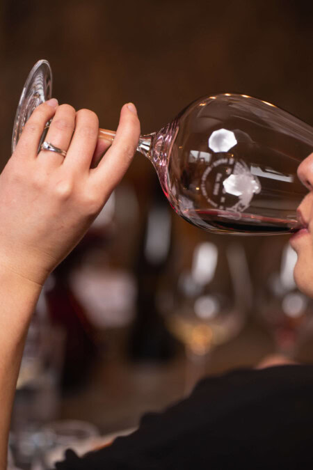 A close up shot of a woman in a black shirt drinking a glass of red wine. 