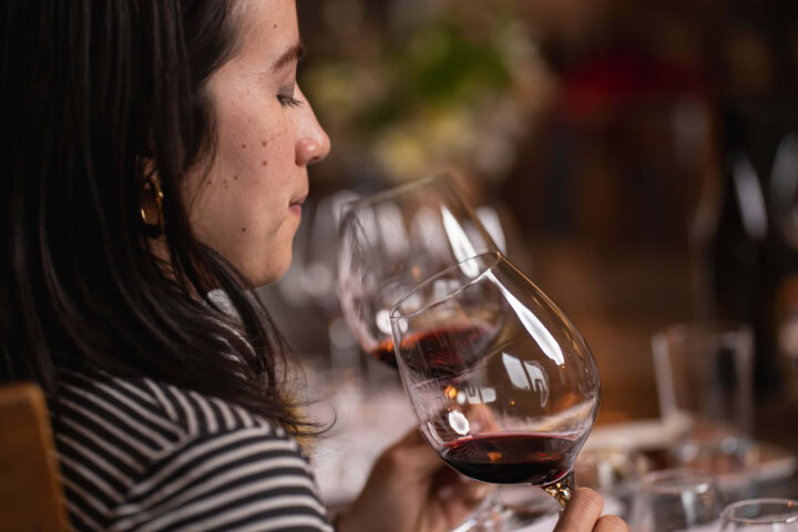 A woman with dark hair wears a black and white striped shirt and pensively sips a glass of Pinot Noir while savoring the tasting experience. 