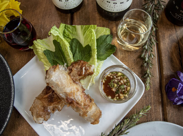 A plate of toasted spring rolls on a bed of lettuce leaves and fresh basil are offered alongside a chili dipping sauce are perfect to serve with a dry Muscat for the lunar new year. 