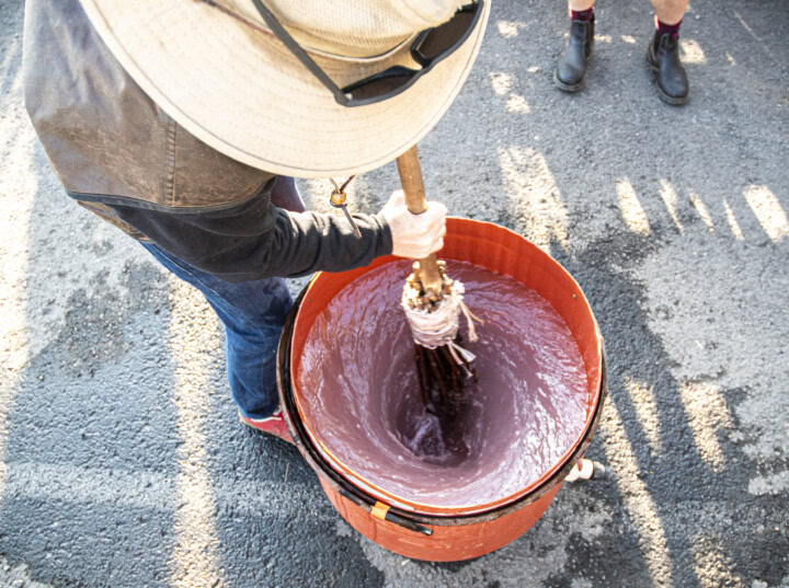 An overhead shot of a winemaker at Brooks Wine in Willamette Valley Oregon wears head-to-toe sun protection uses a hand-made broom to stir a batch of herbal preparations for biodynamic vineyard management.