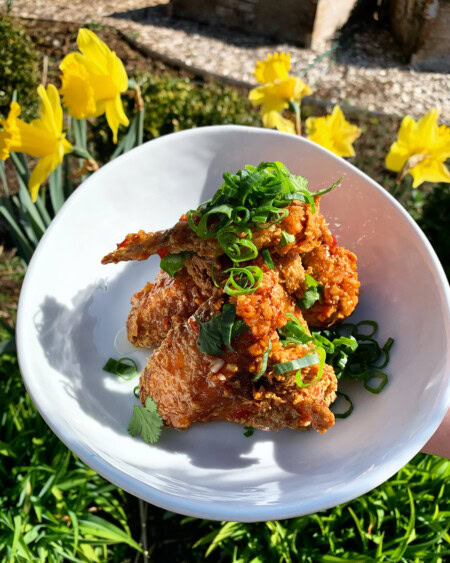 A white bowl sets in the grass in front of yellow daffodils and is filled with a Super Bowl classic game-day food: chicken wings.