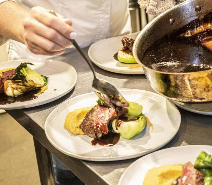 A sauce is spooned over seared duck breasts and steamed bok choy by a chef after being made by deglazing a pan with wine as a cooking technique using wine.  