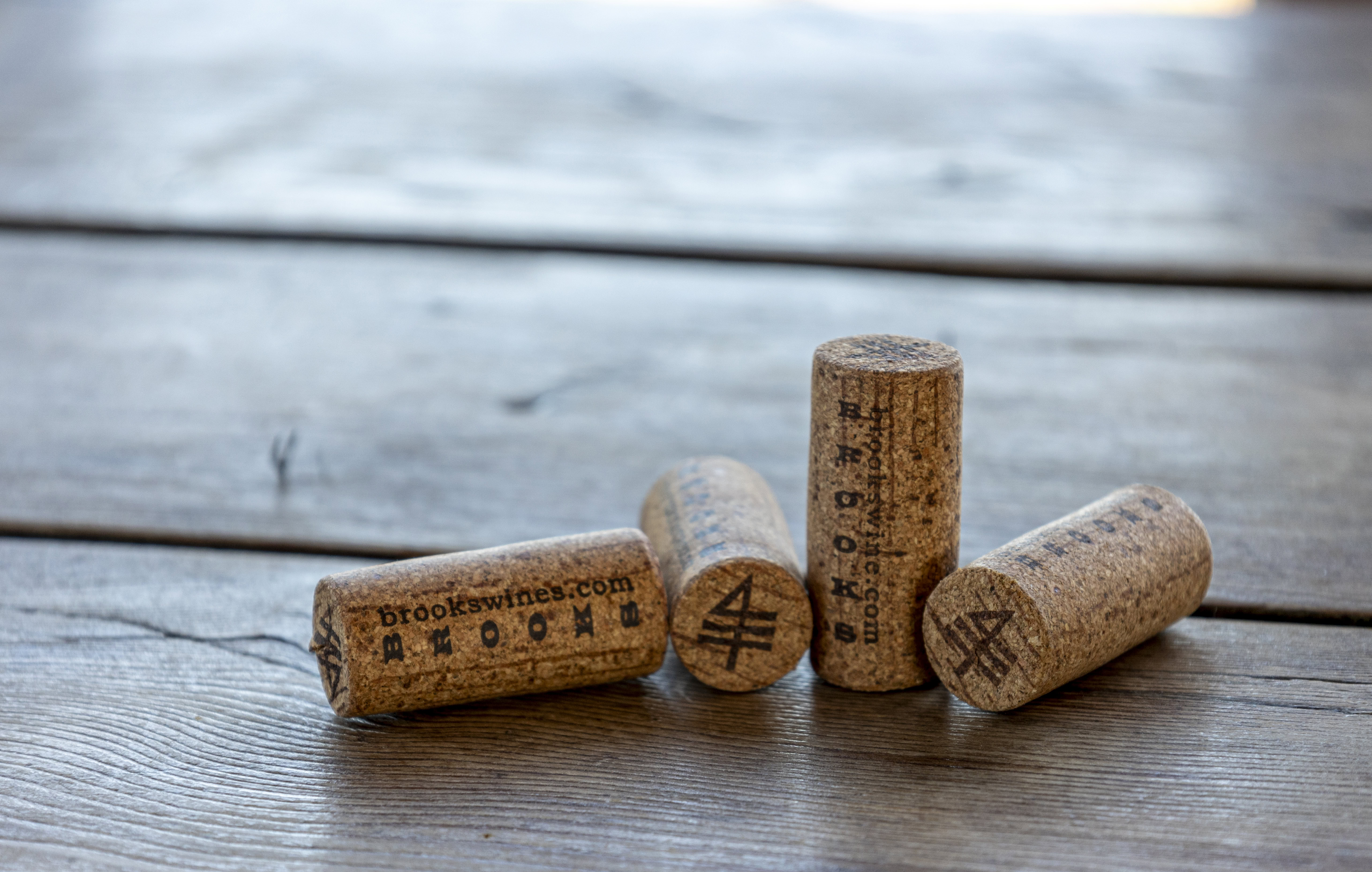 A close up image of a rustic wooden table holding four corks branded with Brooks Wine alchemy symbols for soil.